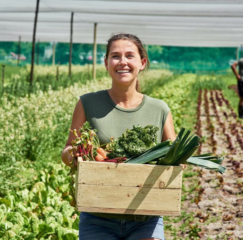 woman harvester holding a wooden crate of fresh vegetables